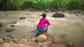 Indonesian woman washes her hands in the river while wearing a pink dress and sitting on the rock inside the village video