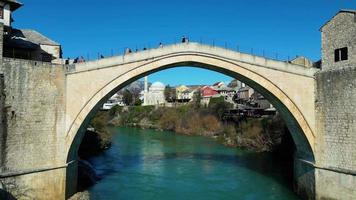 aereo fuco Visualizza di il vecchio ponte nel mostar città nel bosnia e erzegovina durante soleggiato giorno. blu turchese colori di neretva fiume. unesco mondo eredità luogo. persone a piedi al di sopra di il ponte. video