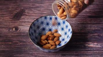 Pouring almond nut in a bowl on table .