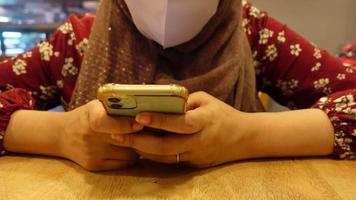 muslim kvinna med ansikte mask använder sig av smart telefon på Kafé video