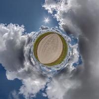 tiny planet in blue overcast sky with beautiful clouds with transformation of spherical panorama 360 degrees. Spherical abstract aerial view. Curvature of space. photo