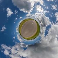 tiny planet in blue overcast sky with beautiful clouds with transformation of spherical panorama 360 degrees. Spherical abstract aerial view. Curvature of space. photo