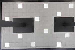 cassette stretched or suspended ceiling with square halogen spots lamps and drywall construction in empty room in house or office with column. Looking up view photo