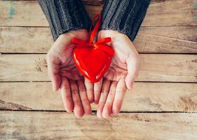 cerca arriba mano mujer participación y persona rojo corazón en madera mesa. enamorado antecedentes. foto