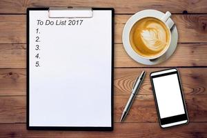 Business concept - Top view clipboard writing To Do List 2017, pen, coffee cup, and phone on wood table. photo