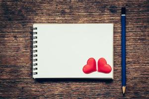 Blank notebook and red heart with pencil on wood background with space. photo