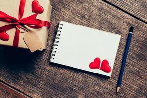 Top view gift box and red ribbon and red heart with notebook for valentine on table wooden. Valentine background. photo