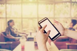 Hand using smartphone and Blurred people in coffee shop with vintage tone. photo