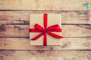 Brown gift box on wooden background. Vintage gift box on wooden background. Gift box with red ribbon on wood background with space. photo