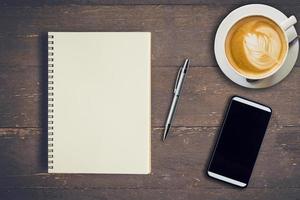 Top view notebook, pen, coffee cup, and phone on wood table, Vintage filter. photo