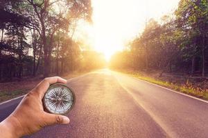 Hand holding compass on empty asphalt road and sunset. photo