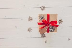 marrón regalo caja y copos de nieve en blanco de madera antecedentes. Clásico regalo caja en de madera antecedentes. regalo caja con rojo cinta en madera antecedentes con espacio. foto