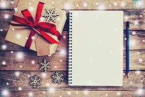 Brown gift box, snowflakes and notebook with snow on wood table for christmas and new year concept. photo