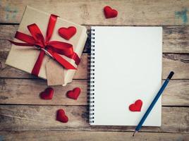 Top view gift box and red ribbon and red heart with notebook for valentine on table wooden. Valentine background. photo