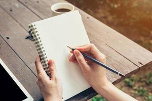 joven negocio mujer mano con lápiz escritura en cuaderno. mujer mano con lápiz escritura en cuaderno y trabajando a café tienda. foto