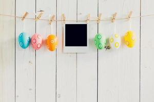 Easter egg and blank photo frame hanging on with white wood with space.