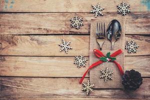 christmas table place setting and silverware, snowflakes, pine cones on wooden background with space. photo
