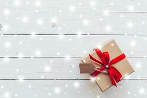 Above brown Gift box and red Ribbon, Snow with tag on white wood background with space. photo