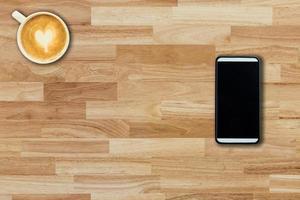 Mobile phone and coffee cup on office wooden table with copy space photo