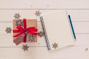 marrón regalo caja, copos de nieve y cuaderno en blanco madera mesa para Navidad y nuevo año concepto. foto