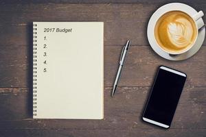 Business concept - Top view notebook writing budget 2017, pen, coffee cup, and phone on wood table. photo