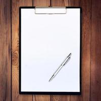 white paper clipboard on wood background with pen photo