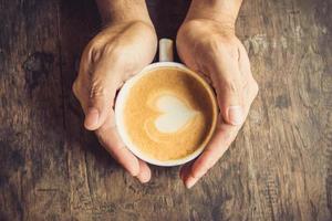 man holding hot cup of coffee, with heart shape photo