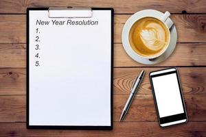 Business concept - Top view clipboard writing New Year Resolution, pen, coffee cup, and phone on wood table. photo