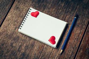 Blank notebook and red heart with pencil on wood background with space. photo