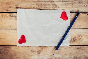 old paper and red heart with pencil on wood background for valentine greeting card. photo