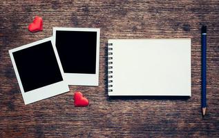 Blank photo frame, notebook, pencil and red heart for valentine on wood table background.