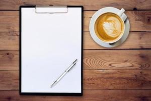 white paper clipboard and coffee on wood background with space photo