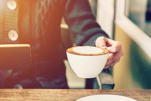 asian woman hand holding coffee and using tablet in coffee shop with vintage toned. photo