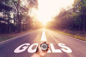 Hand holding compass on Empty asphalt road and Goals concept. photo