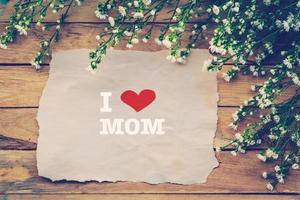 yo amor mamá y contento madres día en marrón papel con blanco flor en de madera tablero foto