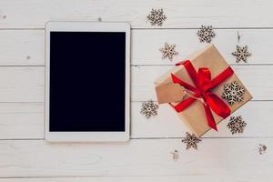 Top view tablet, and gift box with snowflakes on white wood background for christmas and new year. Christmas and New Year Concept. photo