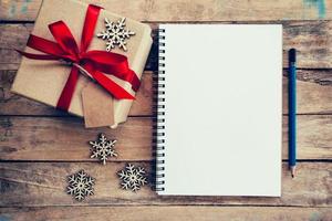marrón regalo caja, copos de nieve y cuaderno en madera mesa para Navidad y nuevo año concepto. foto