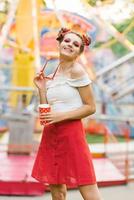 A beautiful young woman walks in an amusement park and holds a paper cup in her hands photo