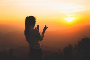 A women is praying to God on the mountain. Praying hands with faith in religion and belief in God on blessing background. Power of hope or love and devotion. photo