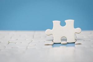 White jigsaw puzzle on a blue background. Completing final task, missing jigsaw puzzle pieces and business concept with a puzzle piece missing. photo