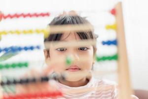 A young cute Asian girl is using the abacus with colored beads to learn how to count at home photo