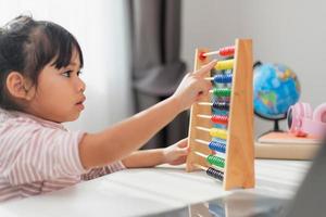 A young cute Asian girl is using the abacus with colored beads to learn how to count at home photo