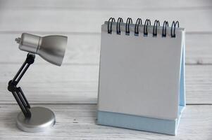 Empty notepad with customizable space for text and ideas. With table lamp on wooden background. Copy space. photo