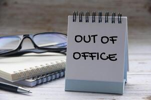 Out of office text on calendar desk with notebook and glasses background. Out of office concept. photo