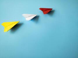 Red paper airplane origami leading white and yellow airplanes on blue background with customizable space for text. Leadership skills concept. photo