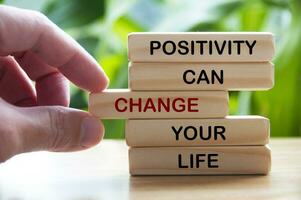 Positivity can change your life text on wooden blocks with hand and blurred nature background. Motivational concept photo
