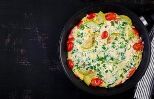 Omelette with tomatoes, zucchini and red onion on dark table.  Frittata - italian omelet. Top view photo