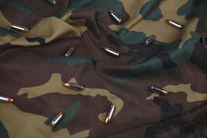 Many pistol bullets and cartridges on dark camouflage background photo