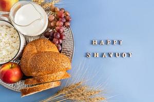 the spring holiday of the Jews of Shavuot. a festive card with traditional food and ears of corn. wooden letters on a blue background - happy shavuot. photo