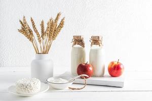 various dairy products, apples and a vase with a bouquet of ears on a white background. front view. the concept of the Jewish holiday of Shavuot. photo